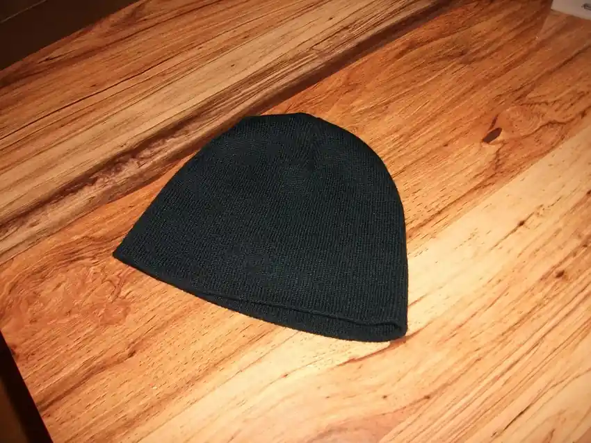 A dark knit cap lying flat on a warm wooden bench top